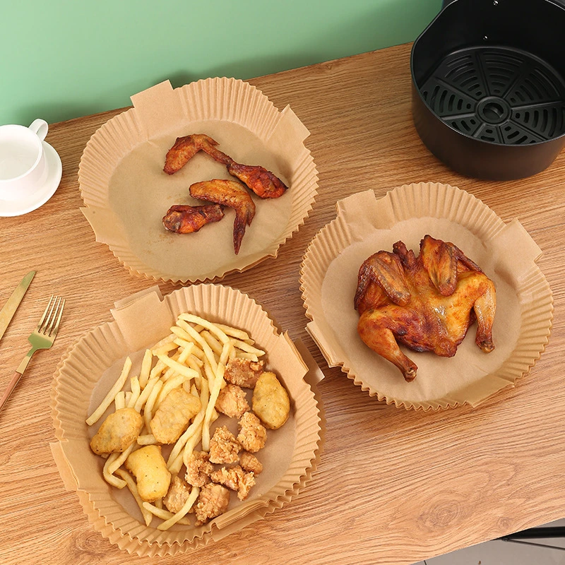 Parchment paper air fryer liners holding chicken wings and fries next to an air fryer