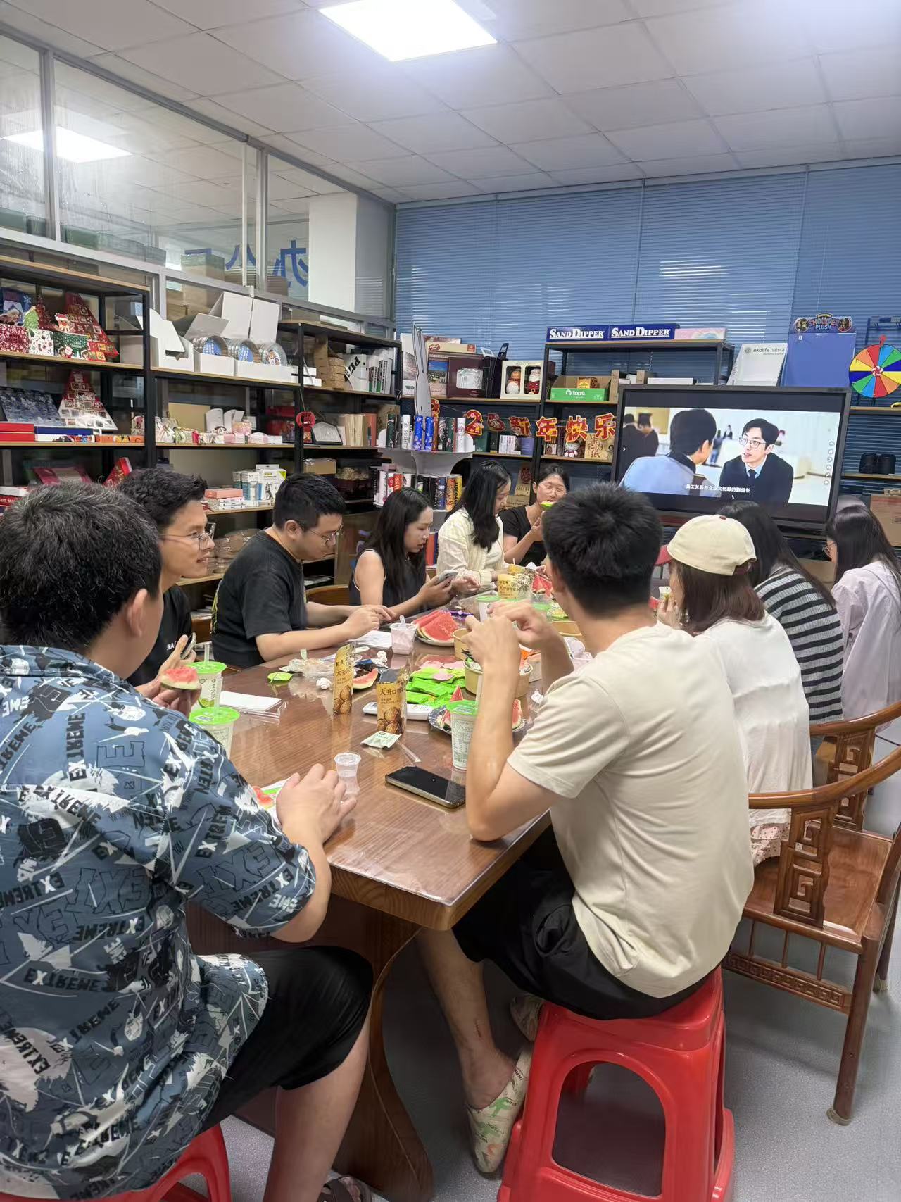 Holidaypac colleagues gathered around a shared table eating watermelon and snacks during the Dragon Boat Festival cultural activity