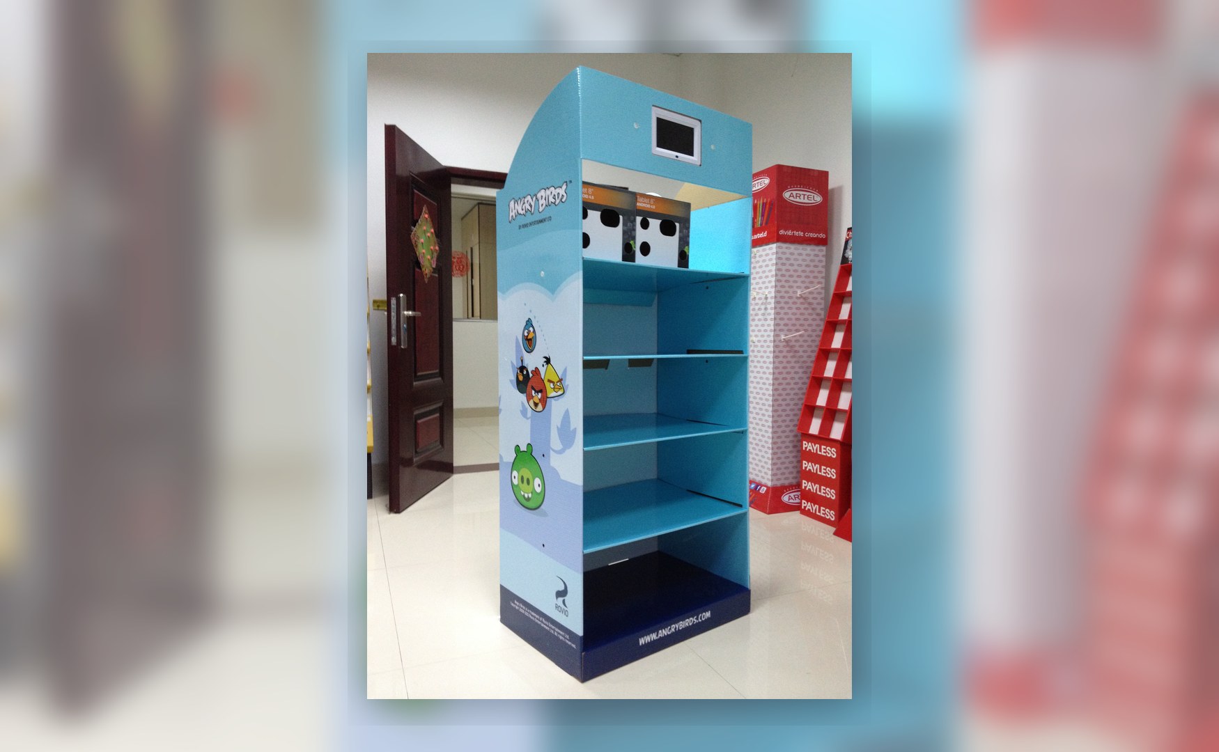 Holidaypacfactory holidaypac factory cardboard display stand with LCD screen side-front angle showing curved header profile, shelves and digital screen integration.