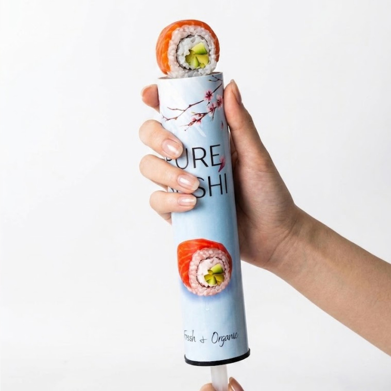 Hand holding sushi push-up paper tube with fresh sushi roll rising from the tube